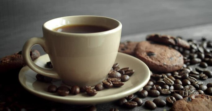 Cup of coffee with cookies and roasted coffee beans scattered on a wooden table. Black coffee mug. Fresh arabica roasted coffee beans. Great start of morning. Espresso, americano, doppio.