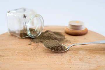black ground pepper in a spoon and a jar of pepper on a wooden background. Container with spices.