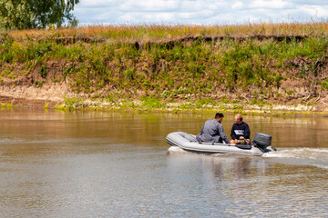 Fishermen sail in an inflatable boat with an outboard motor on a summer river.