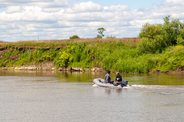 Fototapeta na wymiar Fishermen sail in an inflatable boat with an outboard motor on a summer river.