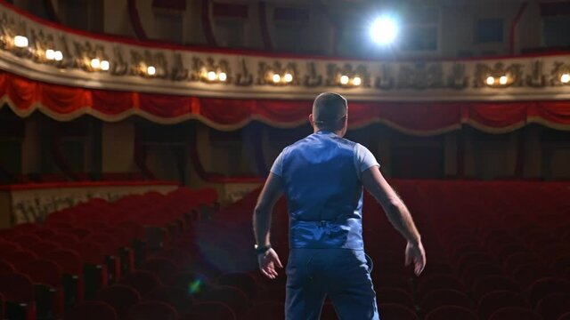 Actor rehearsing his role. Male speaker performing in front of empty auditorium in theater against bright spotlight. Back view.