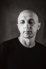 A serious middle-aged man with an unshaven face and a bald head looks thoughtfully to the side. Black and white portrait toned in sepia. Photo taken in studio