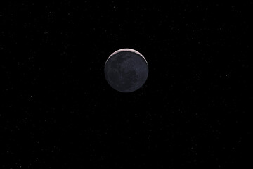 Waxing crescent moon with a night sky stars background. Amazing view of the tiny moon surface illuminated by the sun and the dark side of the moon. Dramatical thin line cut out in the starry nighsky