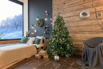 On the eve of the holiday, the interior of the country house is decorated with a New Year tree. large spacious light room decorated with wood with simple wood furniture