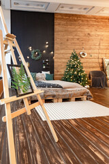 Fototapeta na wymiar On the eve of the holiday, the interior of the country house is decorated with a New Year tree. large spacious light room decorated with wood with simple wood furniture