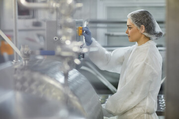 Side view portrait of female worker pushing button while operating machine units at clean food...
