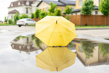 A yellow umbrella is lying in a puddle on the street. Child hid under umbrella, plays after rain