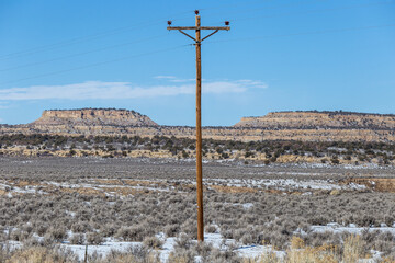 Fototapeta na wymiar Lone telephone pole in center of desert landscape with rocky mountain range and snow covered field on clear day in rural New Mexico
