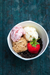 Bowl of various ice cream flavor and crumbled chocolate cookies with strawberry on rustic background.