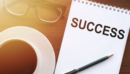 SUCCESS - text on paper with cup of coffee and glasses on wooden background in sinlight.