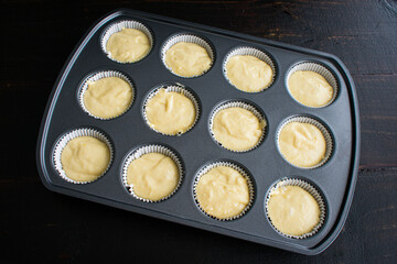 Vanilla Cupcake Batter in a Lined Muffin Tin: Vanilla cake batter poured into a muffin pan lined with paper wrappers
