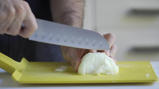 A man chopping onions with a sharp knife over a white table. Indoors, kitchen. 