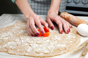 Woman's hands cutting hearts from the dough at home in the kitchen. Homemade pastry. Cooking process. Close-up.