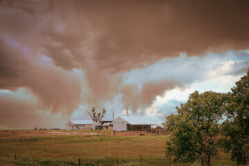 Onimous looking dust storm blowing in over western Oklahoma farm with barns and pasture.