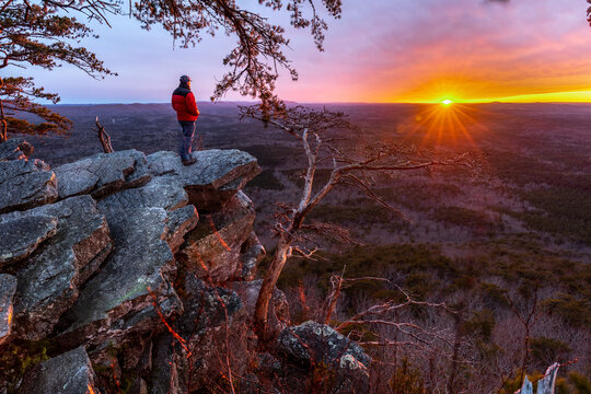 Man, person, standing on the edge of a cliff watching the sun setting on the horizon and a forest valley far below, Pulpit Rock, Cheaha State Park, Alabama