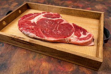 Raw beef ribeye on a round slate plate on an old wooden table in brown tones