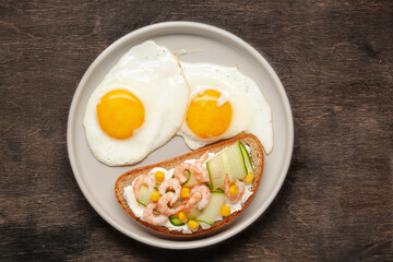 Sandwich with cheese, cucumber and shrimp, fried eggs on a plate and coffee on the table. Healthy breakfast. Top View
