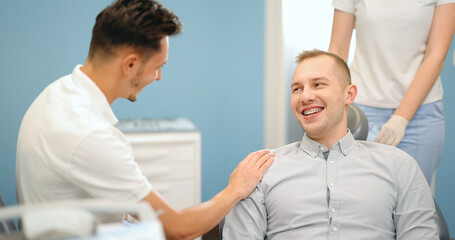 Obraz premium Happy male patient a doctor during a regular orthodontic visit at the dental office. Happy dental treatment concept. 4k video screenshot, please use in small size