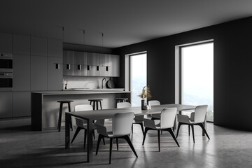 Modern kitchen interior with gray walls, a concrete floor and gray and wooden countertops. A long dining table with chairs near it.
