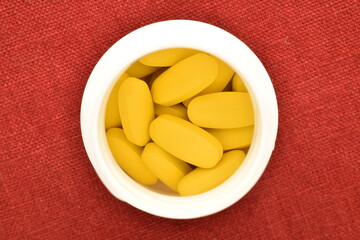 Several oval yellow pills in a plastic box on a red linen cloth, close-up, top view.