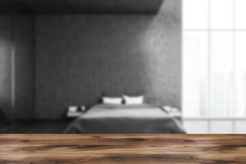 Wooden desk and blurred grey bedroom, bed with linens near window