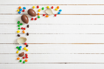 Easter chocolate eggs and candies on white wooden background