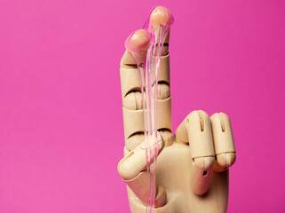 Close-up wooden hand with dripping pink liquid paste pink background. Hair removal and sex concept.