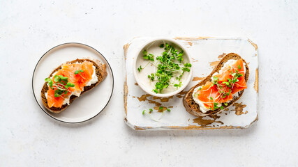 Toasted bread with ricotta (cream cheese), smoked salmon and micro greens served on wooden rustic board. Health care, super food concept. White Stone background. Top view.