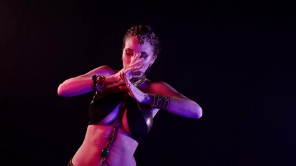A woman dances an oriental belly dance on a dark smoky background in the studio, making beautiful movements. She has an attractive body.
