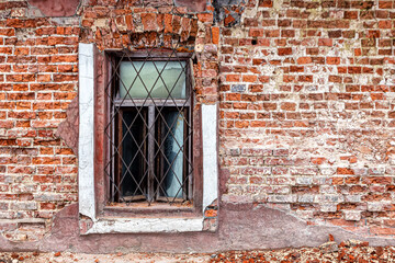 Fototapeta na wymiar Window with a rusty grate on the crumbling brick wall of an abandoned house
