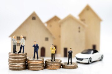 Miniature people:  Businessmen shaking hands on coins stack with house and car.  Concept of investment in housing and vehicles.