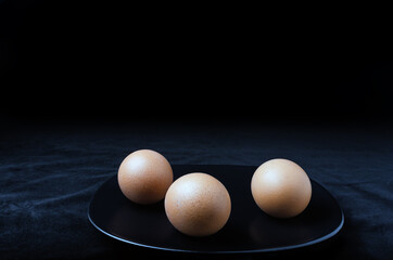 three brown eggs on a black plate, black background. Easter concept