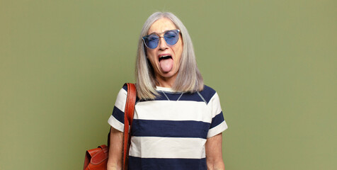 senior woman with cheerful, carefree, rebellious attitude, joking and sticking tongue out, having fun