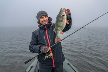 Happy fisherman hold big perch fish at boat with tackle. Success fishing at wild lake