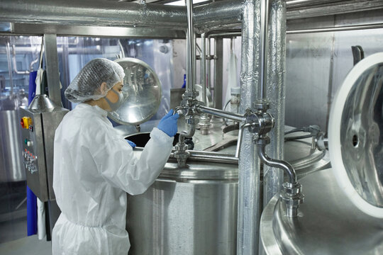 Side view portrait of young woman wearing mask and protective wear while working at food factory, copy space