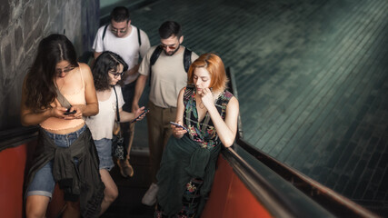 Group of friends talk on smartphones while standing on escalator. Modern people with cell phones...