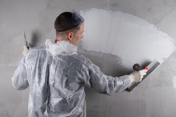 a master in a protective suit is working on leveling the concrete wall with a large spatula,...