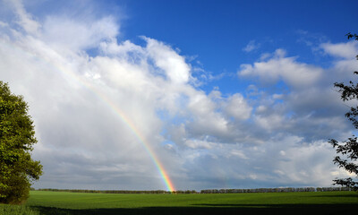 A blurry rainbow over a green field against a blue sky