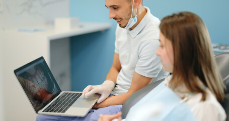 Dentist showing photo of teeth on a laptop for a young patient during an orthodontic treatment. Girl having a consultation with an orthodontist. 4k video screenshot, please use in small size