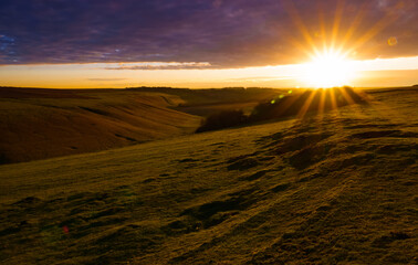 Sunset corona illuminates a deep English valley with grass fields glowing green, amber and red under a blanket of thick winter cloud