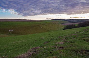 looking down a long English valley with fields green grass, red soil and purple winter woodland...