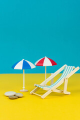 Beach relaxation and vacation concept. Toy sun lounger and umbrella on colorful paper background.
