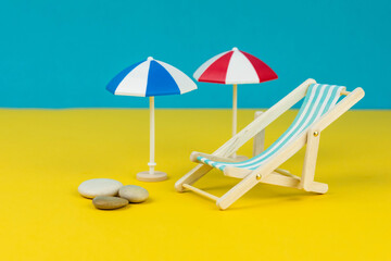 Beach relaxation and vacation concept. Toy sun lounger and umbrella on colorful paper background.
