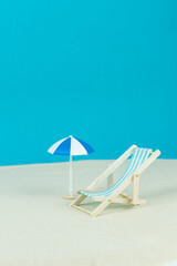 Beach relaxation and vacation concept. Toy sun lounger and umbrella on sand and colorful paper background.