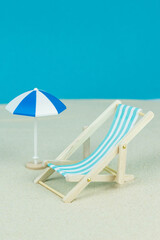 Beach relaxation and vacation concept. Toy sun lounger and umbrella on sand and colorful paper background.