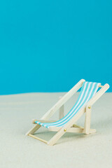 Beach relaxation and vacation concept. Toy sun lounger on sand and colorful paper background.
