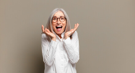 senior woman feeling shocked and excited, laughing, amazed and happy because of an unexpected...