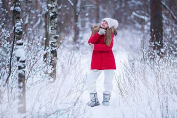 Beautiful little girl wearing red jacket and knitted hat playing in a snowy winter park. Child playing with snow in winter. Kid play and jump in snowy forest.