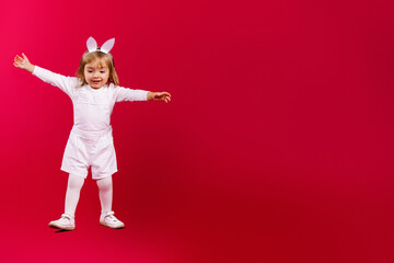 Full-length photo of pretty baby girl wearing Easter bunny ears and white costume, jumping on red background with plenty side space for text: sale, discount, advertisement