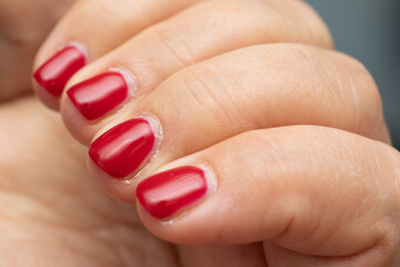 Lady's nails with bright red nail polish in which regrowth can be seen, concept of the need for a new manicure